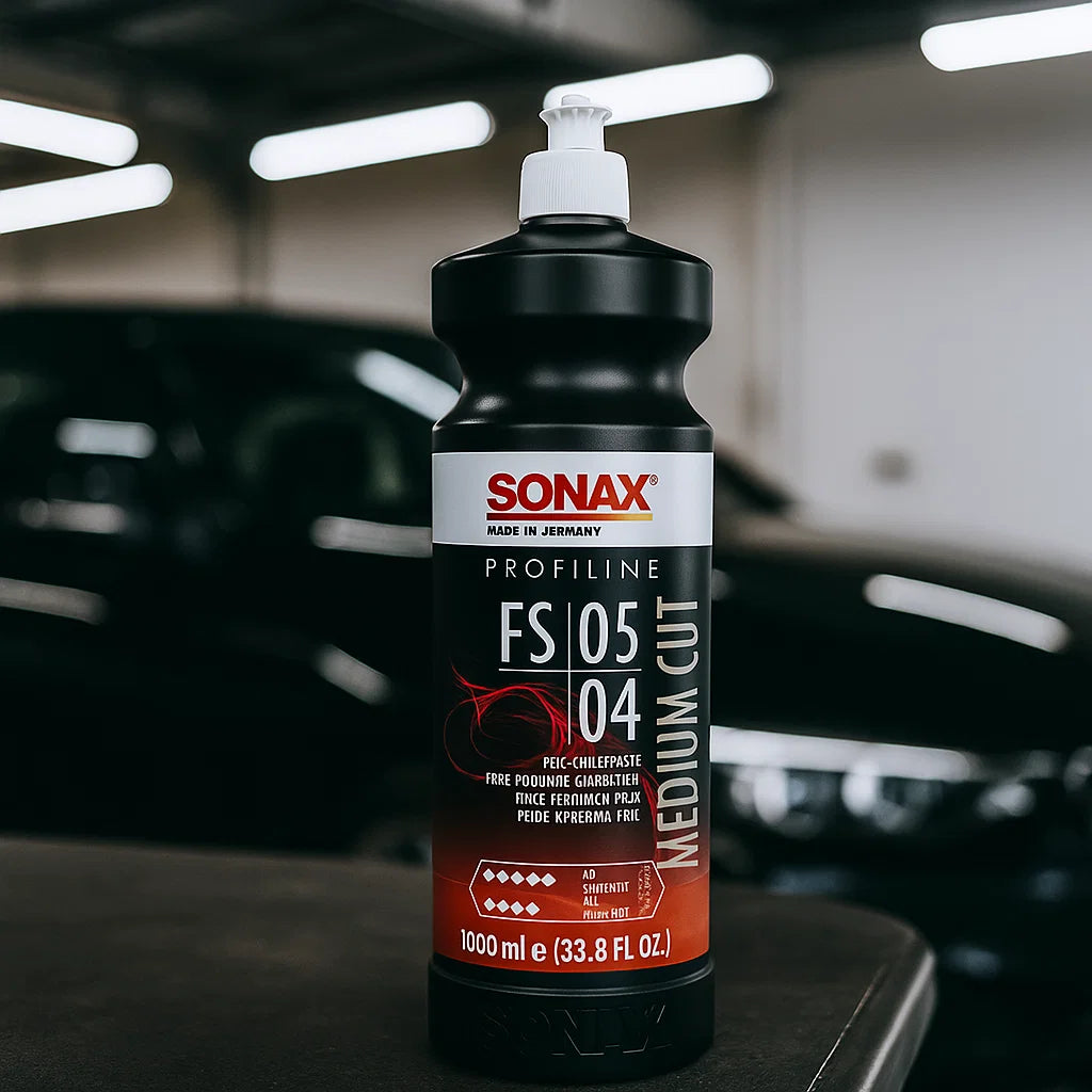 Flasche Sonax Profiline FS 05-04 Medium Cut Politur (1000 ml) in einer Aufbereitungshalle vor einem Fahrzeug.