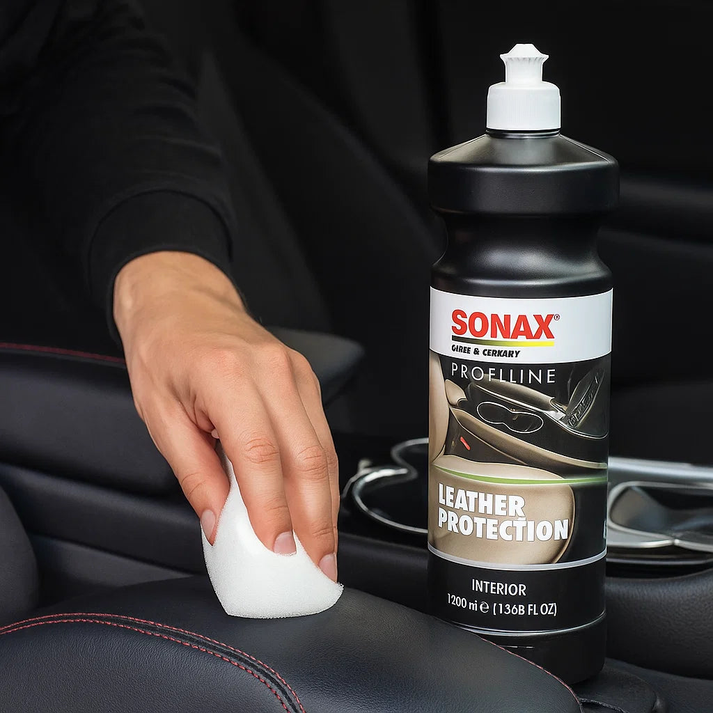 Fahrzeugaufbereiter trägt Sonax Leather Protection mit einem Applikationsschwamm auf eine schwarze Lederarmlehne im Innenraum auf