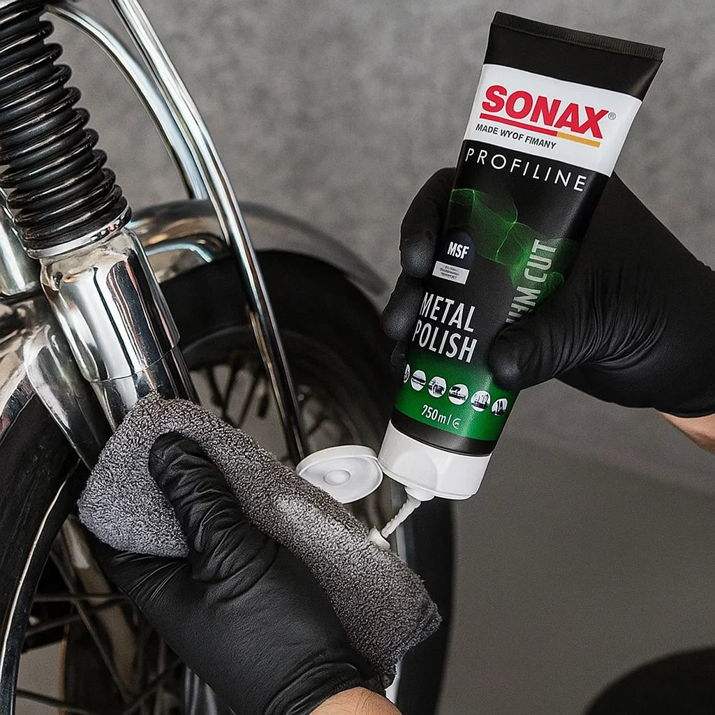 Fahrzeugaufbereiter trägt Sonax Profiline Metal Polish mit einem Mikrofasertuch auf ein verchromtes Motorradteil auf, um die Oberfläche zu polieren und aufzufrischen