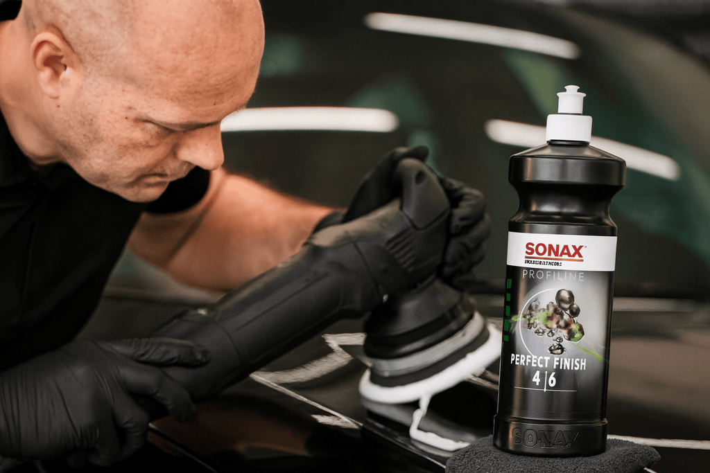 Professioneller Fahrzeugaufbereiter poliert die Motorhaube eines schwarzen Autos mit einer Poliermaschine und SONAX Profiline Perfect Finish 4/6.