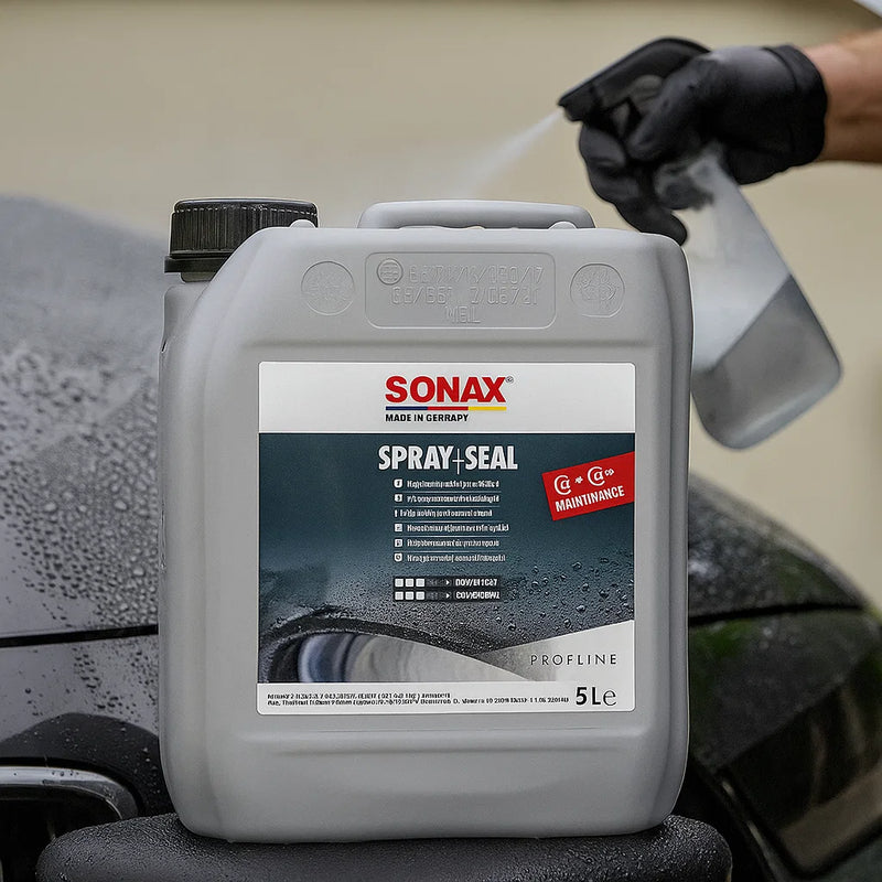5-Liter-Kanister Sonax Profiline Spray+Seal bei der Anwendung – im Hintergrund sprüht ein Fahrzeugaufbereiter das Versiegelungsmittel auf den nassen Lack eines Fahrzeugs