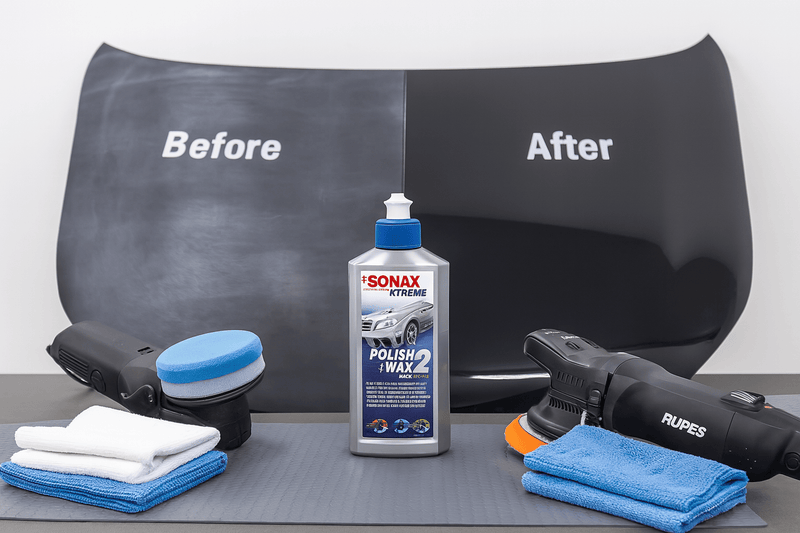 Ein aufgeräumter Poliertisch mit Poliermaschinen, Mikrofasertüchern und der SONAX XTREME Polish+Wax 2 Flasche im Zentrum. Im Hintergrund eine Motorhaube mit deutlichem Vorher-Nachher-Effekt: links verwitterter Lack, rechts glänzend polierte Oberfläche mit Tiefenglanz.